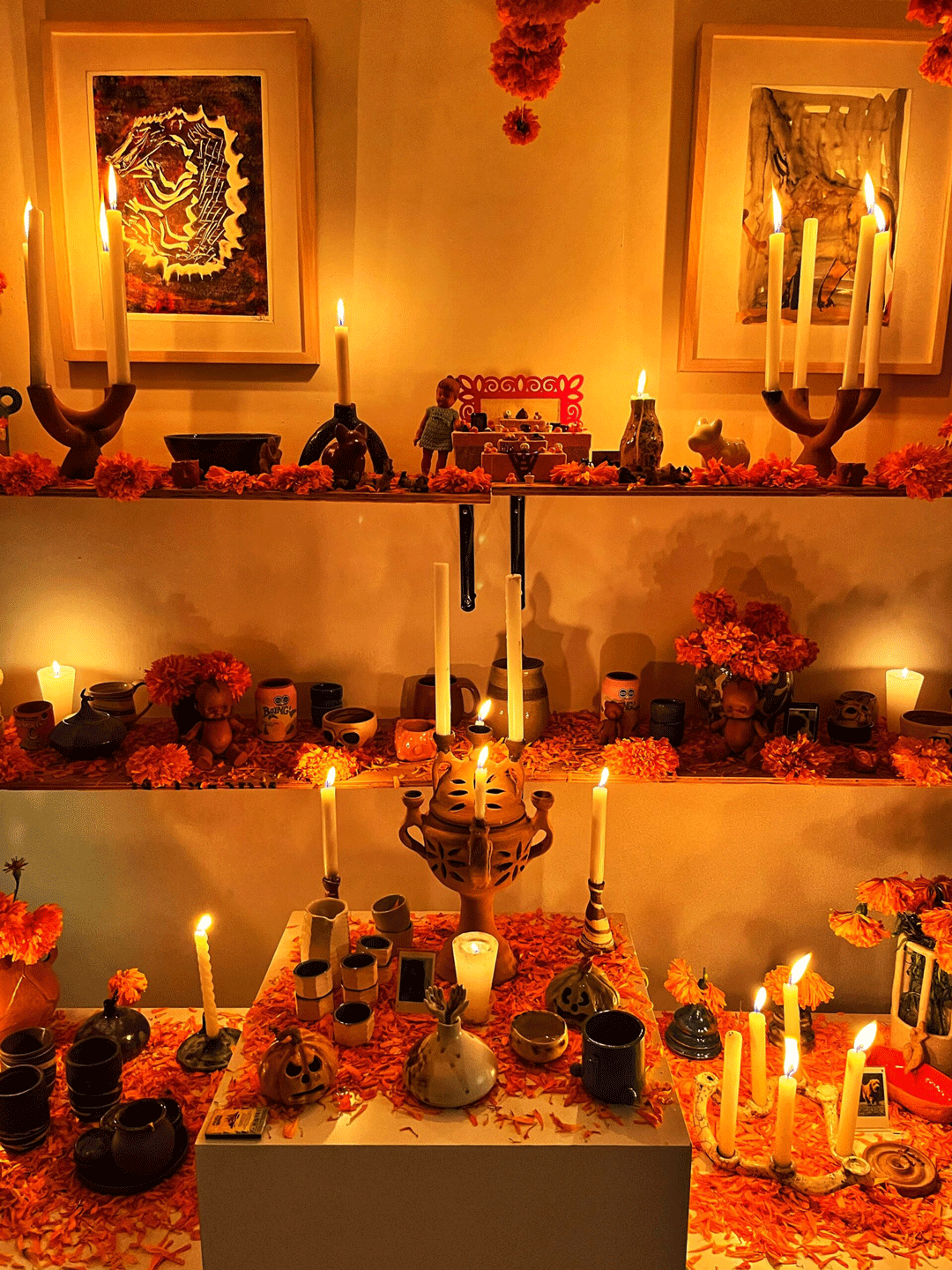 Ofrenda de tres pisos con piezas de cerámica iluminadas por velas.
