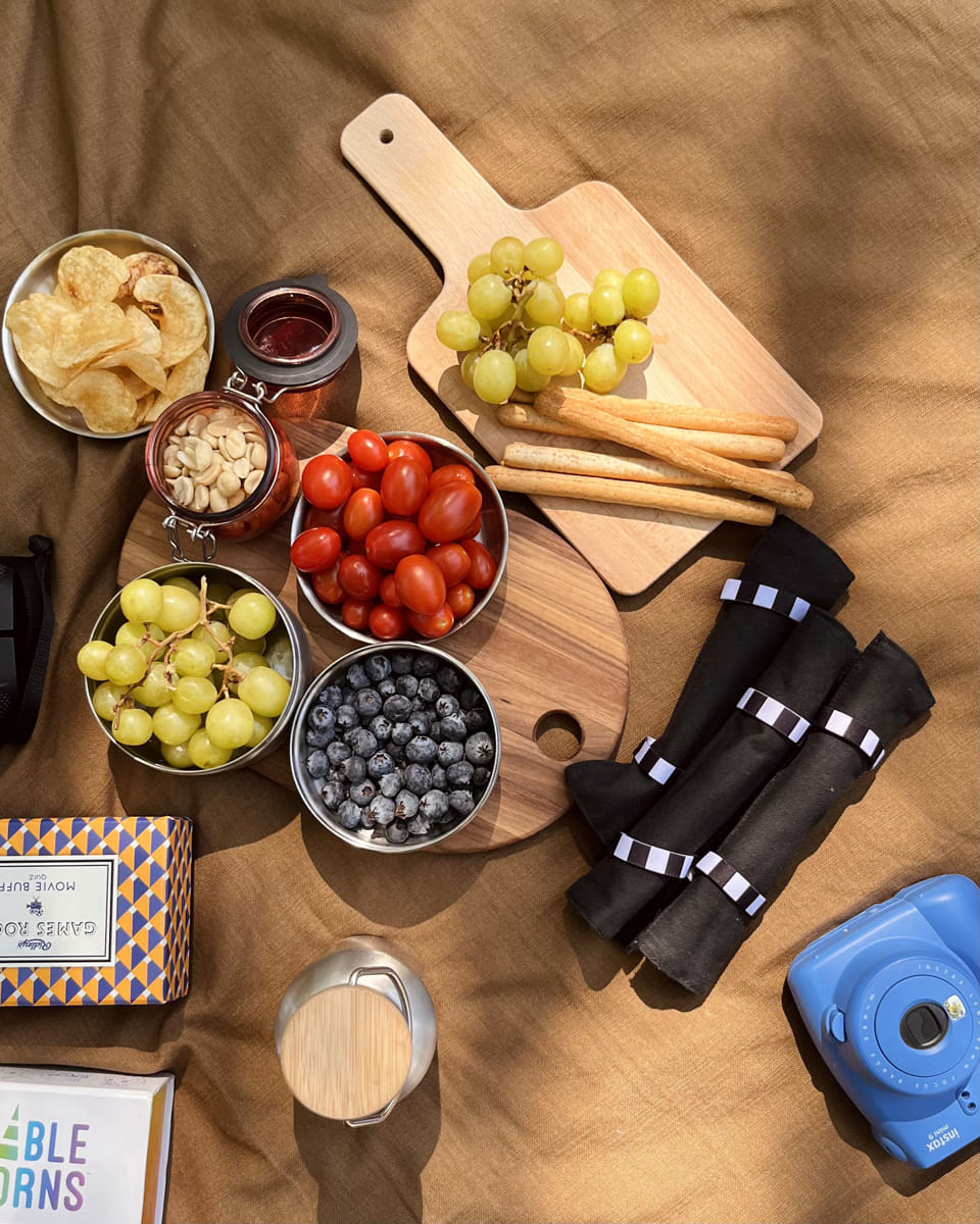Tablas de madera con papas, jitomates cherry y blue berries, encima de un mantel café sobre el césped.