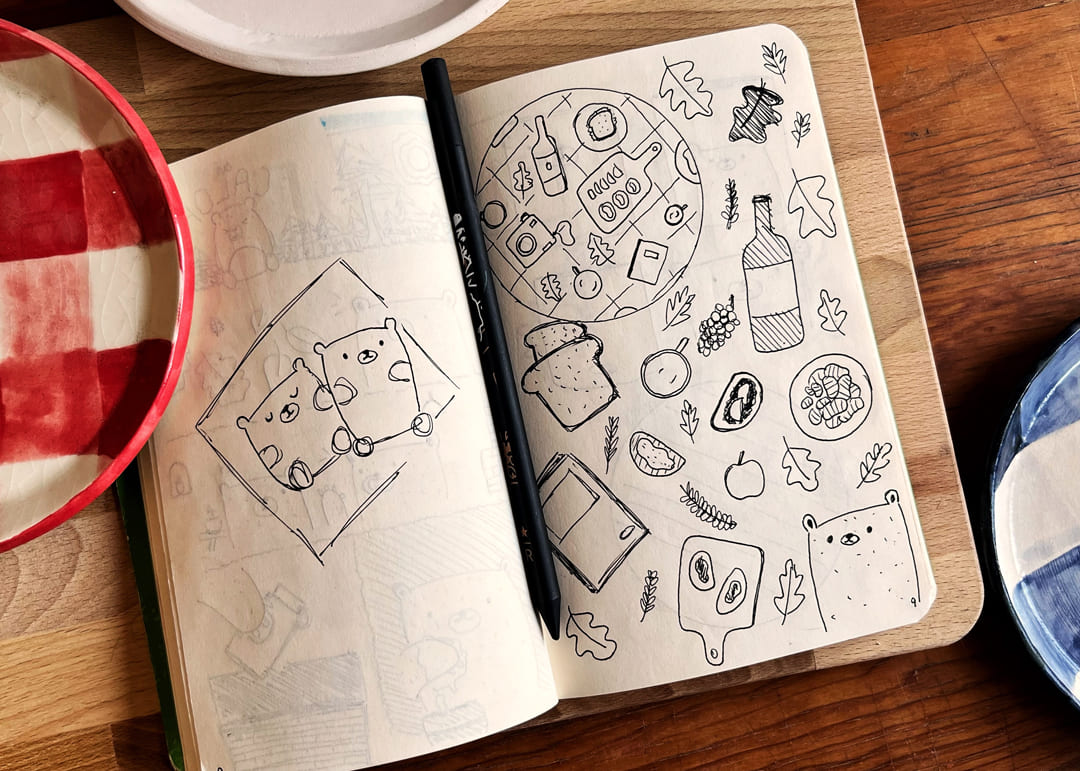 Libreta con un boceto dibujado a mano de un Plato Picnic, acompañado de dibujos de comida y bebidas.